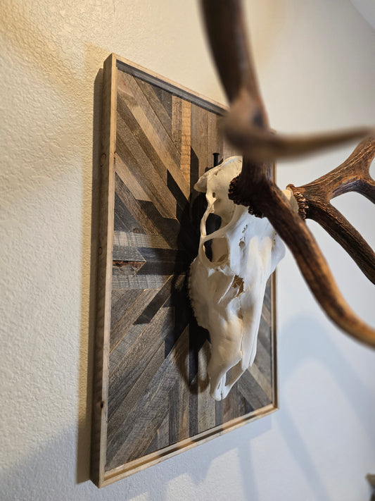 Decorative wall art with elk antlers and skull on a wooden frame.