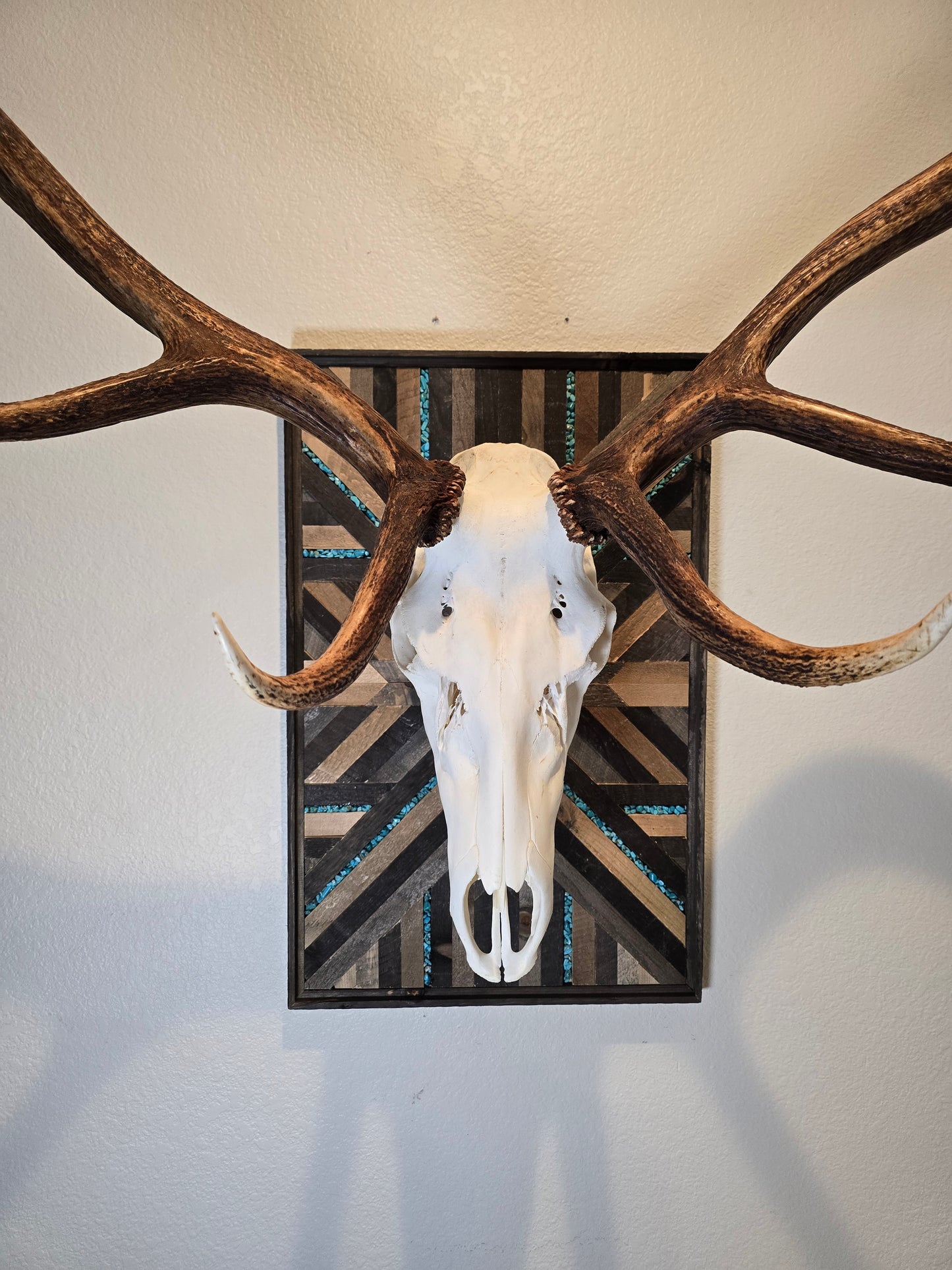 Decorative wall art with elk antlers and skull against a geometric-patterned background.