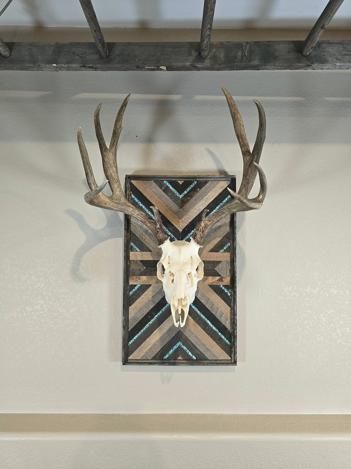 A mounted deer skull on a wall plaque with a geometric pattern, featuring turquoise inlay and wood elements.